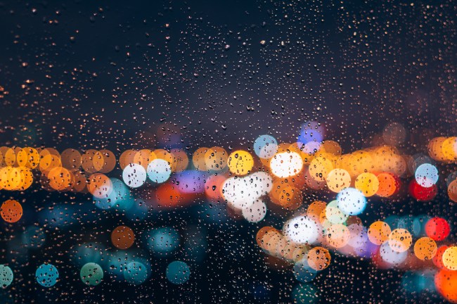 Defocused view of colorful lights through rainy glass, close-up view