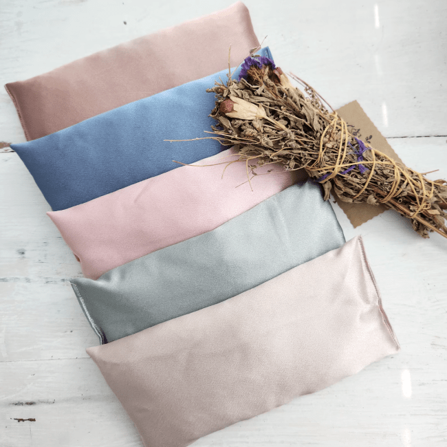 Five pastel satin eye pillows next to a bundle of sage