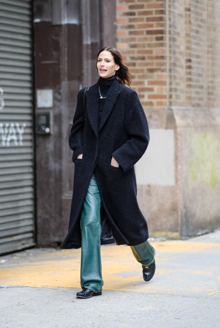 A guest wears a black turtleneck, a black long coat, green leather pants, and loafers during NYFW on February 10, 2024.