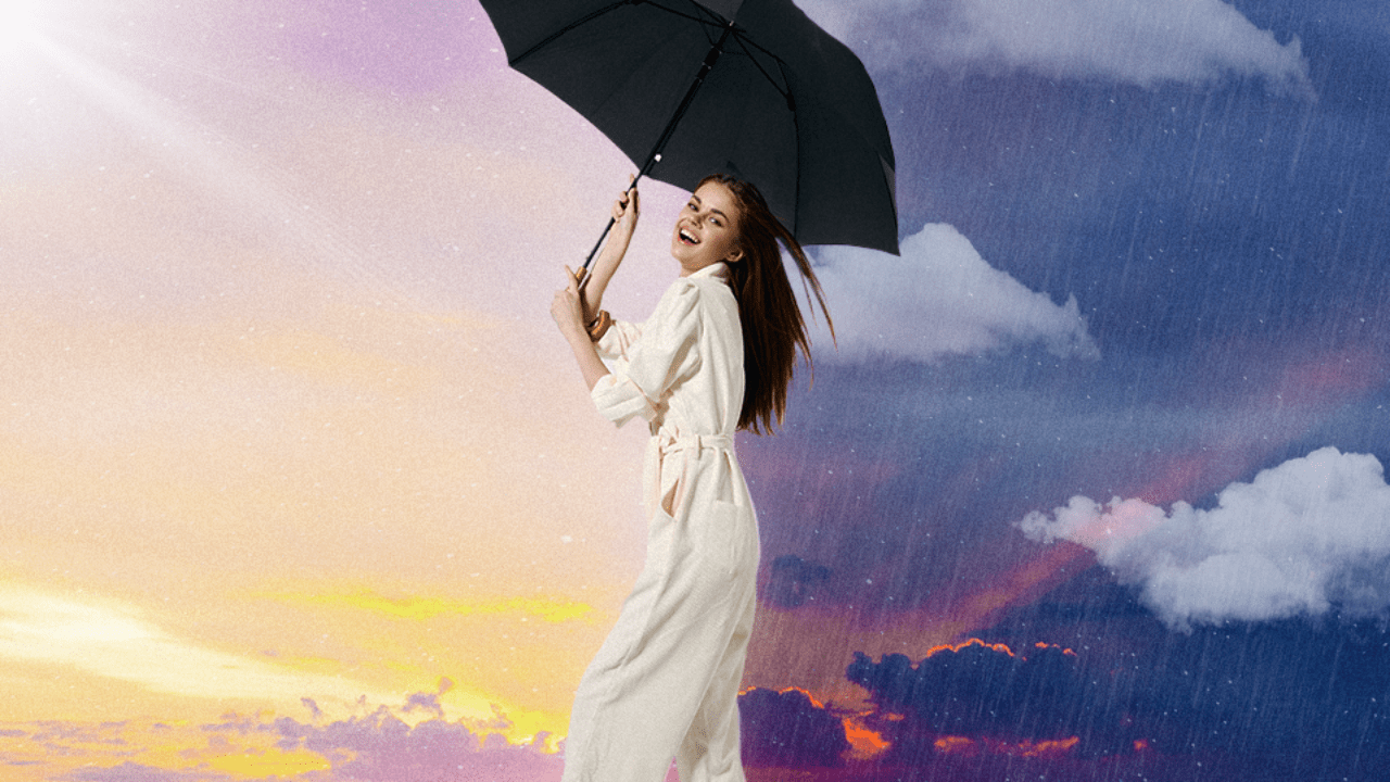 A woman laughing while holding an umbrella in front of a sky that is part sunny and part rainy