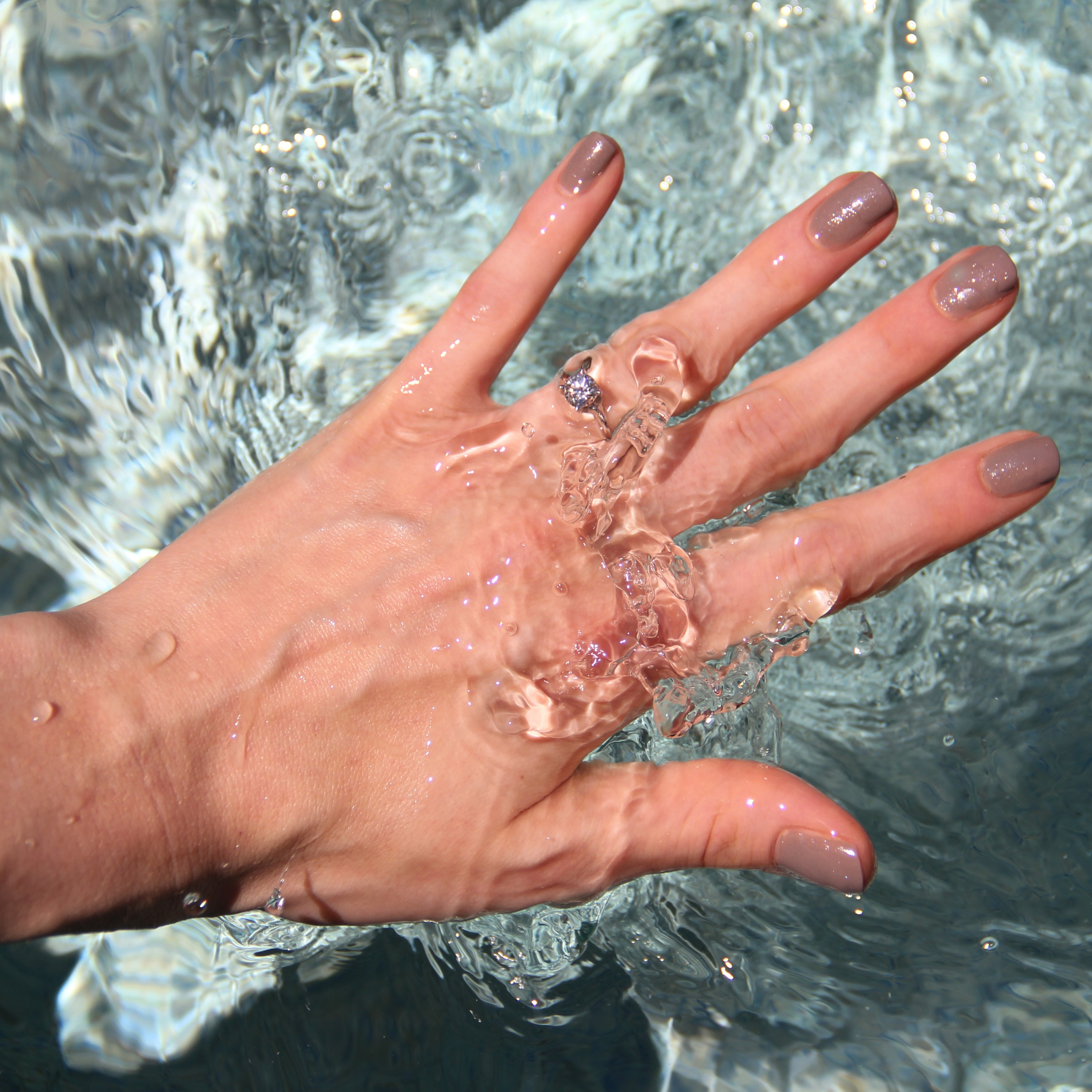 Surface level view of woman's hand plunging in water.