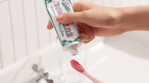 A hand squeezing Euthymol's Pink Whitening Toothpaste onto a pink toothbrush over a white sink