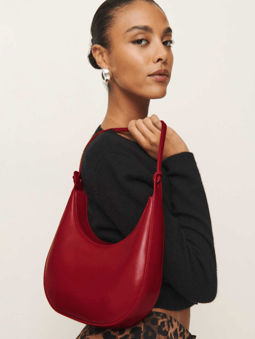A model carrying Reformation's Medium Rosetta Shoulder Bag in Lipstick Red