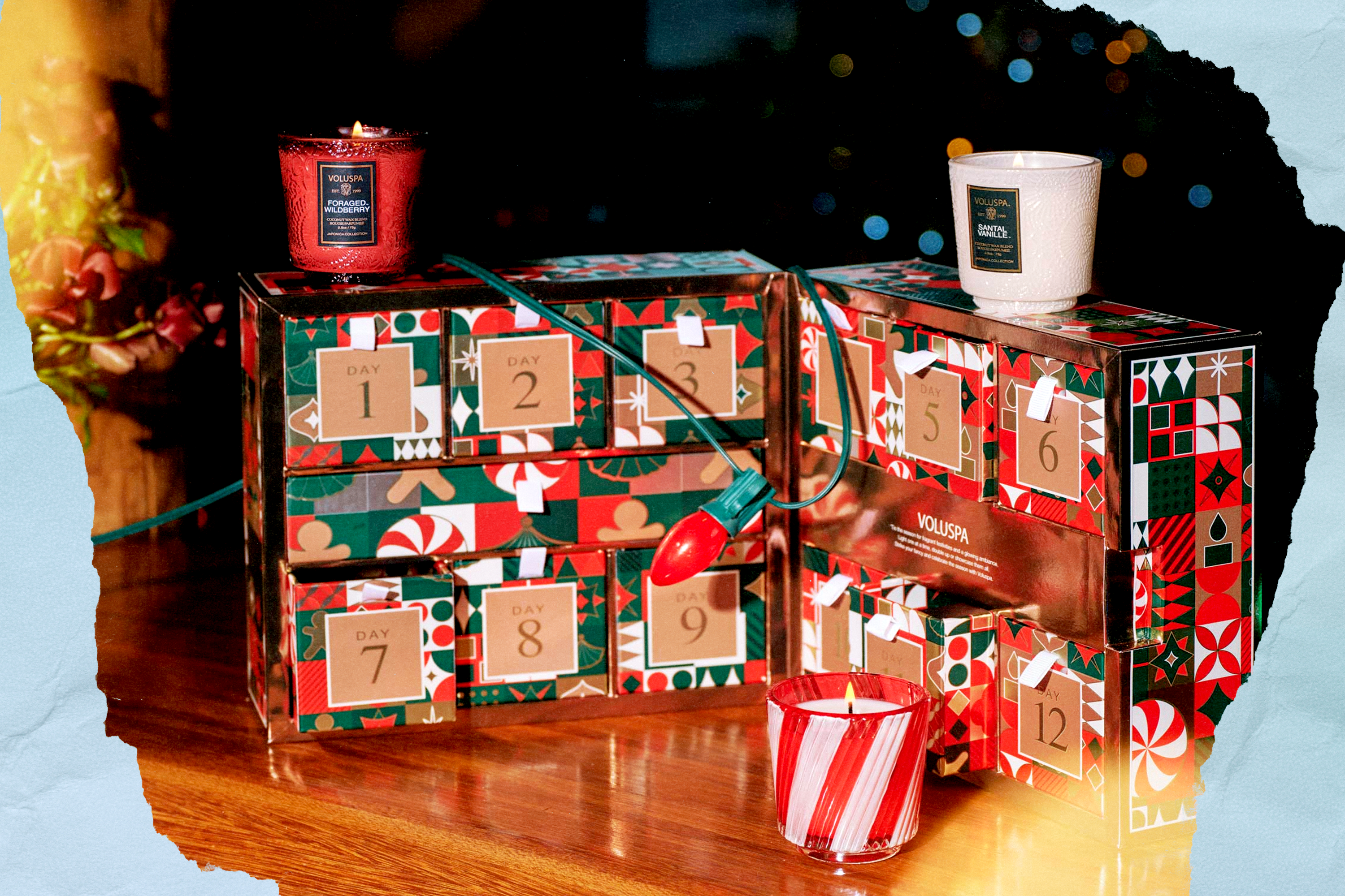 A ifestyle shot of Voluspa's 2025 advent calendar on a wooden table with Christmas lights wrapped around it