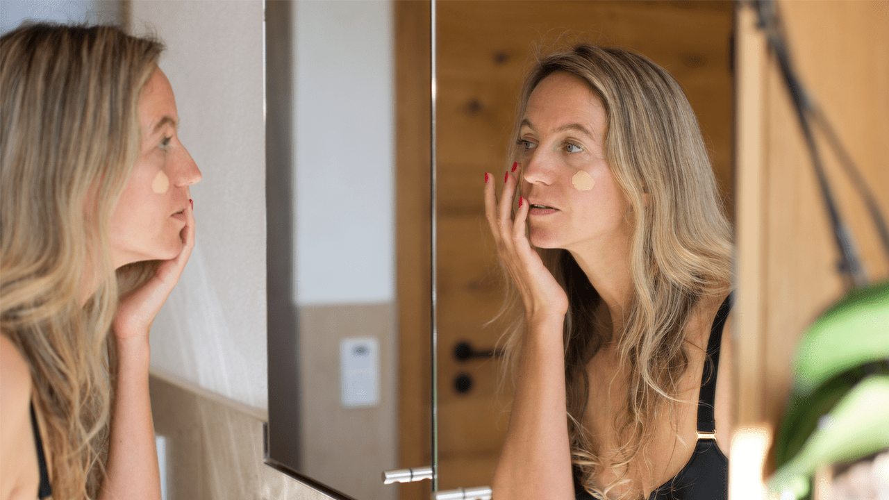 A woman applying foundations to her face with her finger in the bathroom mirror