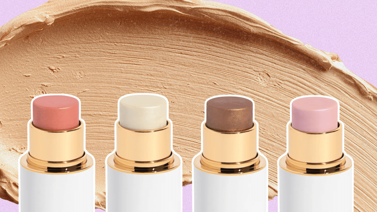 A pink background with a foundation smear and four different face sticks in blush, highlighter, and bronzer tones.